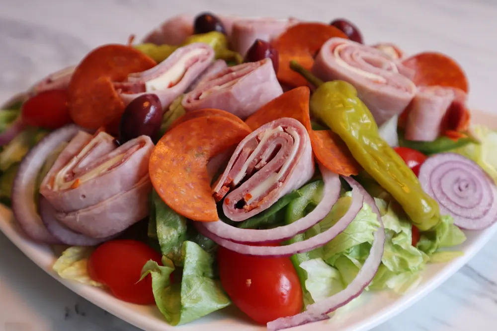 A fresh Mediterranean salad with greens, tomatoes, olives and cured meats